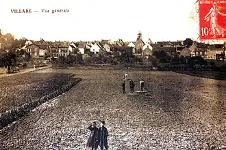 Vue d'un village en arrière-plan d'un champ sur une carte postale ancienne.