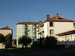 Photographie de logement HLM : au premier plan, un immeuble de trois étages rose clair et derrière, un immeuble de cinq étages vert pâle.
