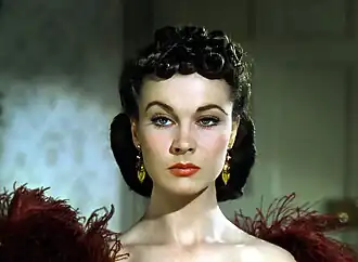Une femme à l'épaule dénudée, avec une coiffure complexe. Elle lève un sourcil d'un air agacé.
