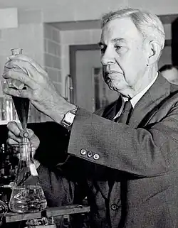 Photo en noir et blanc d'un septuagénaire en costume manipulant de la verrerie de laboratoire.