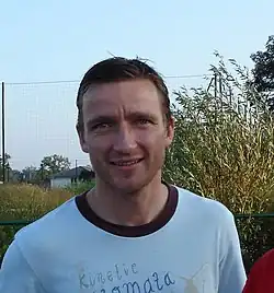 Portrait d'un homme portant un T-shirt blanc à col noir. Une incription figure sur ce vêtement.