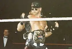 Un catcheur avec une ceinture de champion à la taille retire une veste en cuir.
