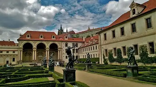 Un jardin à la française, orné de statues, entouré par plusieurs corps de bâtiments Renaissance, en pierre de taille claire, aux toits de tuiles. La cathédrale sur une hauteur à l'arrière plan.
