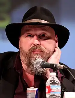 Un homme barbu et coiffé d'un chapeau à larges bords s'adresse à une foule lors d'une convention.