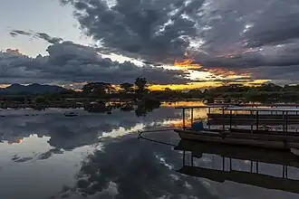 Réflexion dans l'eau d'un coucher de soleil avec des nuages gris et orange au-dessus du Mékong, et deux pirogues amarrées à la berge à Don Det.
