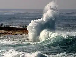 Une lame se brisant et déferlant sur une jetée.