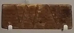 Morceau de bois gravé des lettres W et N.