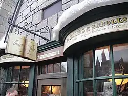 Devanture d'un magasin dans les tons vert et beige, dont la pancarte suspendue à une potence représente un livre ouvert