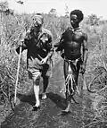 Un autochtone, Raphael Oimbari, aide un soldat australien blessé, George Whittington, durant la campagne de Nouvelle-Guinée. Les auxiliaires autochtones sont célébrés par les Australiens comme étant des «&nbsp;anges aux cheveux crépus&nbsp;» (en)