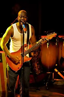 Un homme noir chantant et tenant une guitare sur scène.