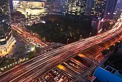 Pont autoroutier surplombant des voies routières dans un environnement urbain dense (de nuit)