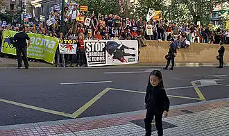 Au premier plan une petite fille, et en arrière-plan des manifestants tenant diverses banderolles.
