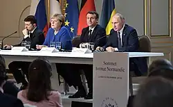 Quatre dirigeants installés à une table devant un parterre d'auditeurs, avec les drapeaux de leurs pays respectifs en arrière-plan.