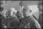 Un détenu de Sachsenhausen avec des lunettes au premier plan porte un emblème d'identification bicolore