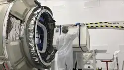 Deux personnes tenant le Cold Atom Laboratory devant un vaisseau Cygnus.