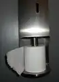 Distributeur vertical de papier toilette, avec déroulement du rouleau dans le sens anti-horaire.